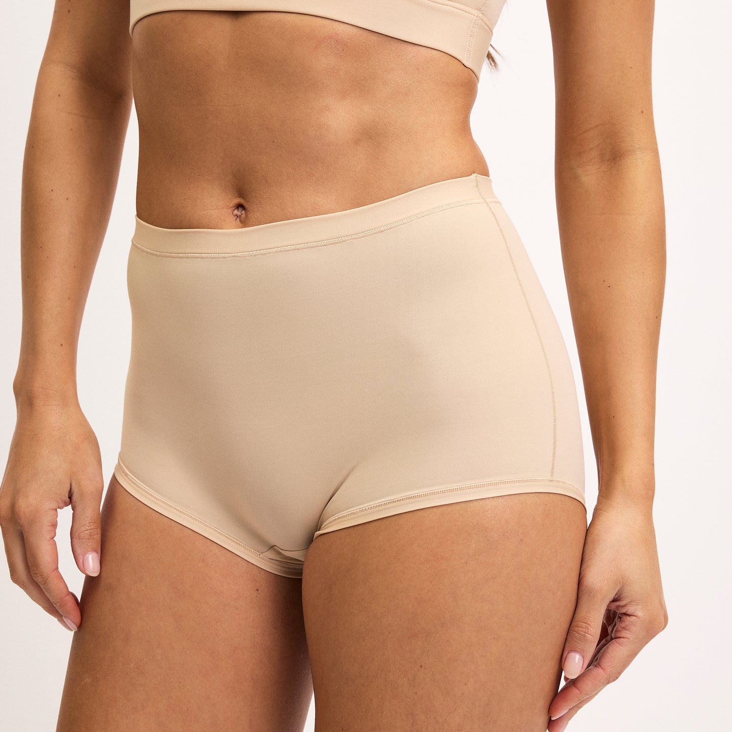 On a white studio backdrop, Darion wears the Bliss Boyshort in Beige, featuring a smooth high-rise fit with soft microfiber fabric and full coverage through the hips and back.
