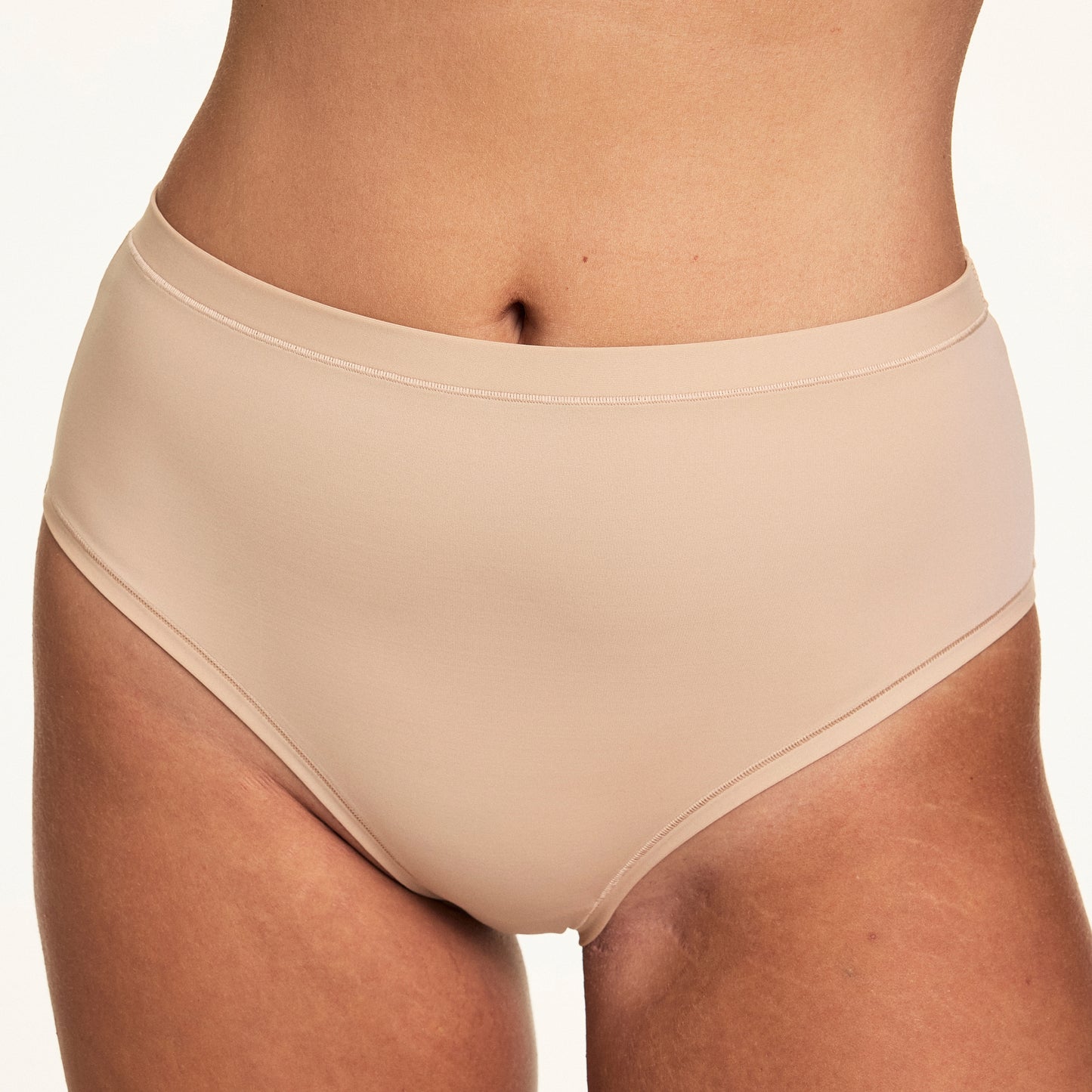 On a white studio backdrop, Sonnie wears the Bliss Highwaist Brief in Beige, featuring a smooth high-rise silhouette with soft microfiber fabric and clean no-show edges.