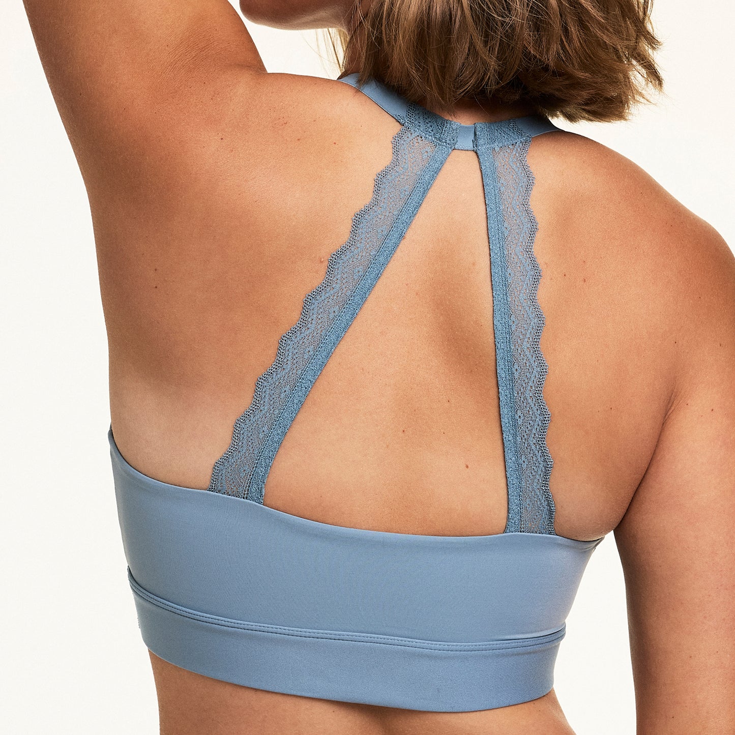 On a white studio backdrop, Sonnie wears the Bliss Lace Halterneck Bralette in Poolside, shown from the back with soft lace halter straps, a keyhole racerback detail, and a smooth microfiber band.
