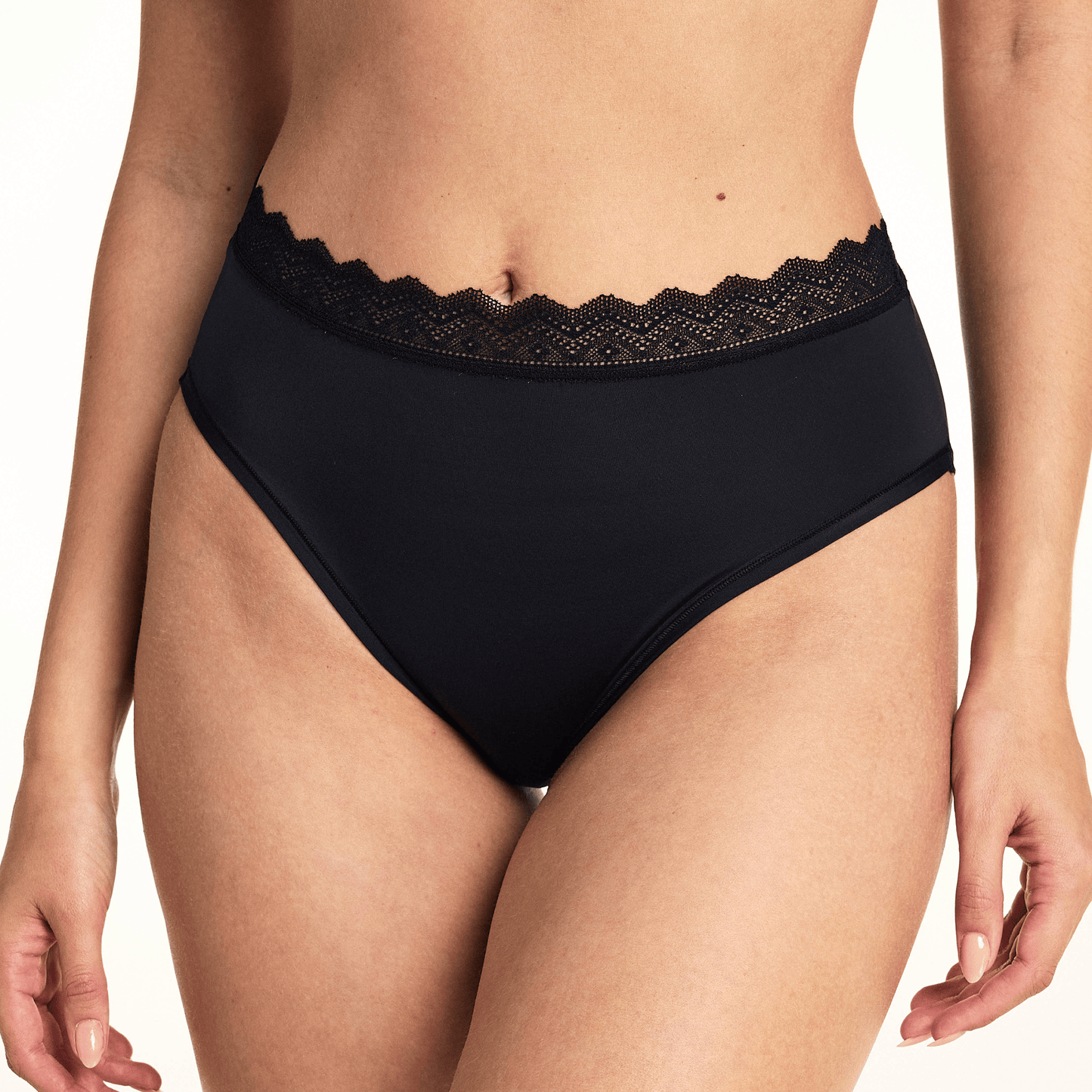 In a studio setting, Laura wears the Bliss Lace Highwaist Brief in Black, highlighting the high-rise silhouette, smooth microfiber fabric, and scalloped lace waistband with cheeky back coverage.