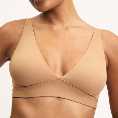 Close-up on a light studio backdrop of Amber wearing the Bliss Plunge Adjustable Bralette in Tan. The wireless bralette features a deep V neckline, wide straps, and ultra-soft microfiber fabric designed for smooth everyday comfort.