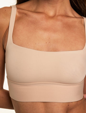 Close-up on a light studio backdrop of Gianna wearing the Bliss Square Neck Bralette in Beige. The longline bralette features a square neckline, thin straps, and ultra-soft microfiber fabric with wireless support.