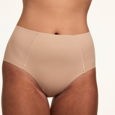 Close-up on a light studio backdrop of Sonnie wearing the Invisible No-Show Highwaist Brief in Beige. The high-rise brief features smooth raw-edge edges, soft microfiber fabric, and a no-show design made to disappear under clothing.