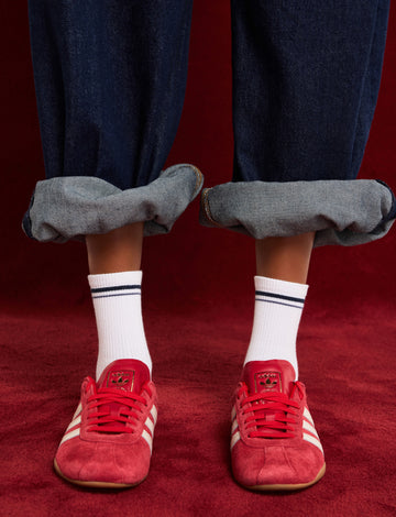 On-model shot of cream ribbed crew socks, styled with pink sneakers and rolled light denim.