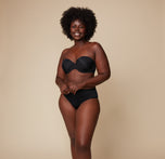 Akesha smiles warmly while wearing the Base Strapless Bra in Black paired with matching high-waist briefs against a neutral backdrop.