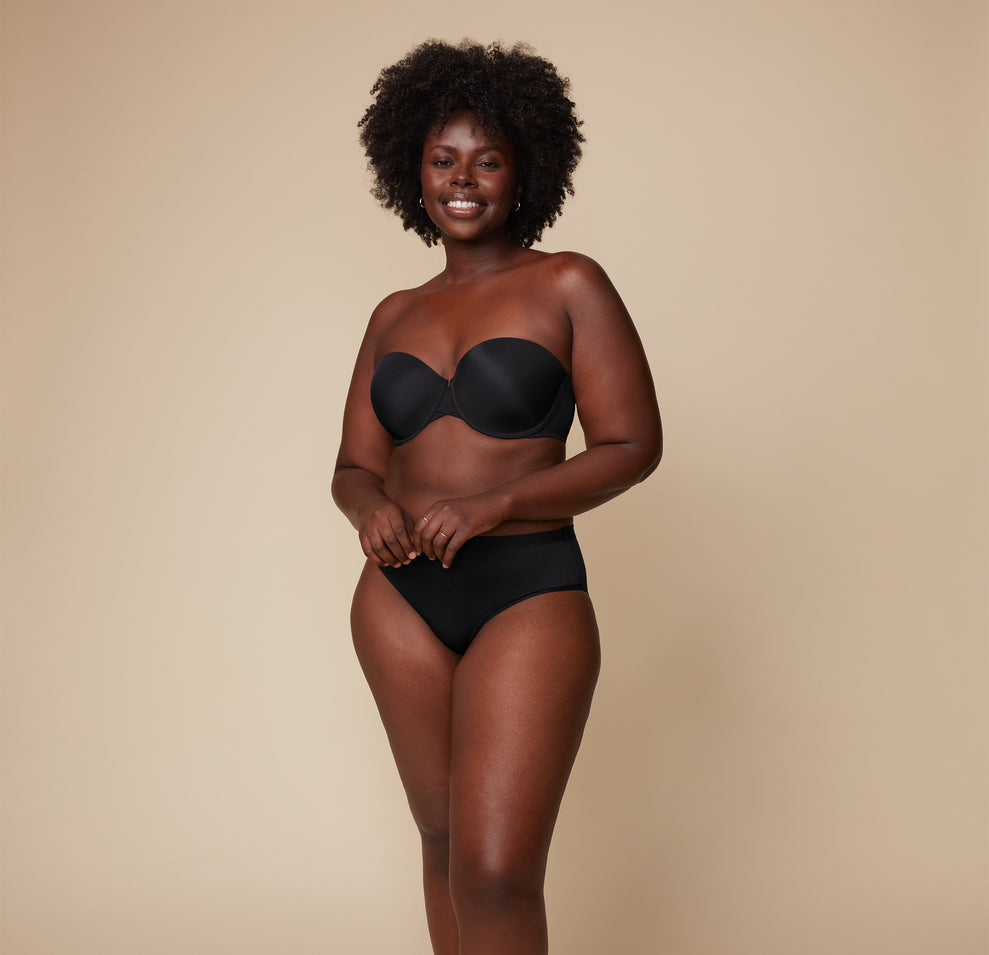 Akesha smiles warmly while wearing the Base Strapless Bra in Black paired with matching high-waist briefs against a neutral backdrop.
