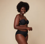 Akesha poses turned slightly to the side while wearing the Base Strapless Bra in Black, emphasizing the bra’s comfort and fit.