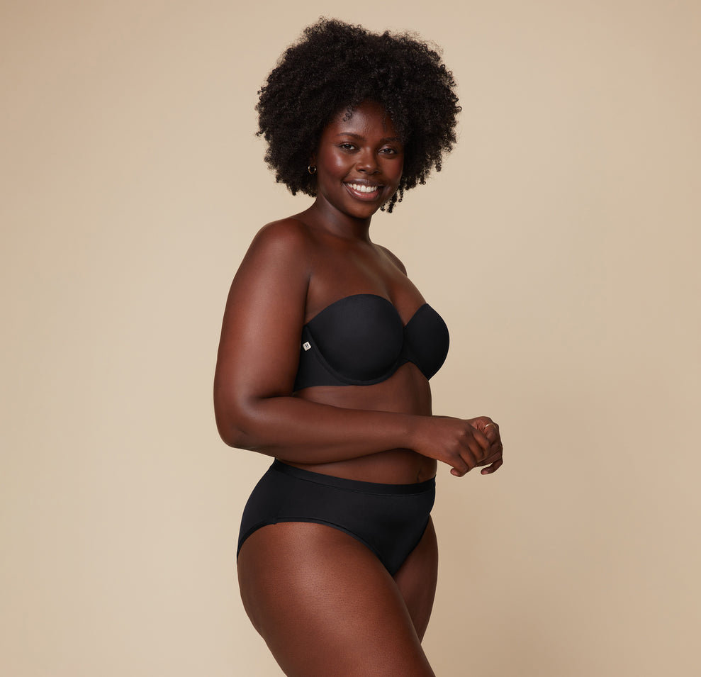 Akesha poses turned slightly to the side while wearing the Base Strapless Bra in Black, emphasizing the bra’s comfort and fit.