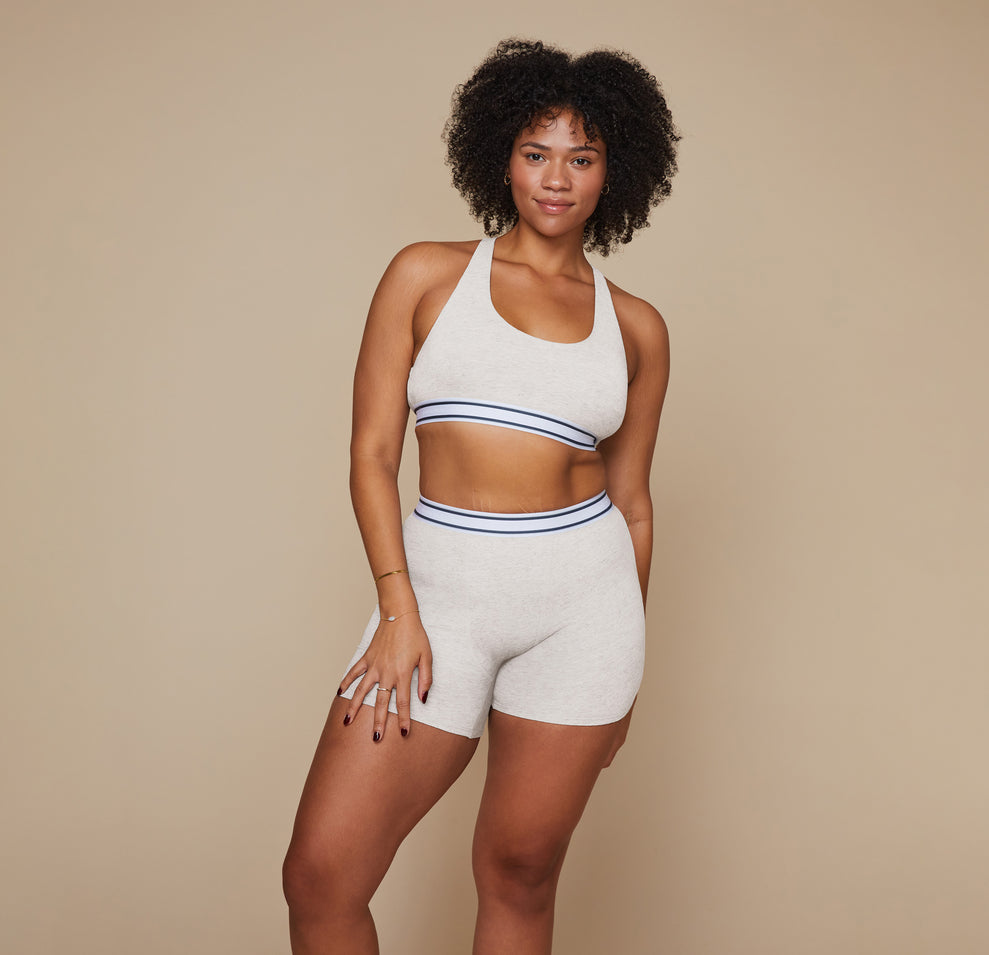 Model standing with her arms at her side wearing the Cloud Cotton Logo Racerback Bralette and matching Cloud Cotton Logo Boxer Brief in the color Heather Oatmeal.