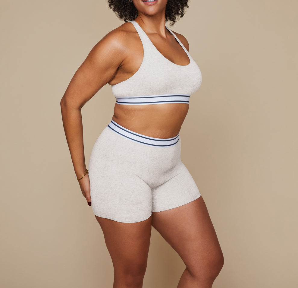 Model standing with her arms at her side wearing the Cloud Cotton Logo Racerback Bralette and matching Cloud Cotton Logo Boxer Brief in the color Heather Oatmeal.
