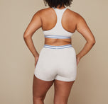 Model standing with her back to the camera wearing the Cloud Cotton Logo Racerback Bralette and matching Cloud Cotton Logo Boxer Brief in the color Heather Oatmeal.