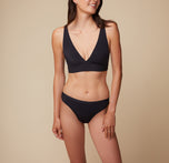 Front view of model Anna in the Bliss Plunge Adjustable Bralette and Bliss Bikini in Black, with arms at her sides, highlighting the classic bikini cut of the underwear.