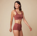 Anna is captured at a slight angle, smiling, while wearing the Lounge Rib Scoop Bralette and Lounge Rib Boyshort in Clay.
