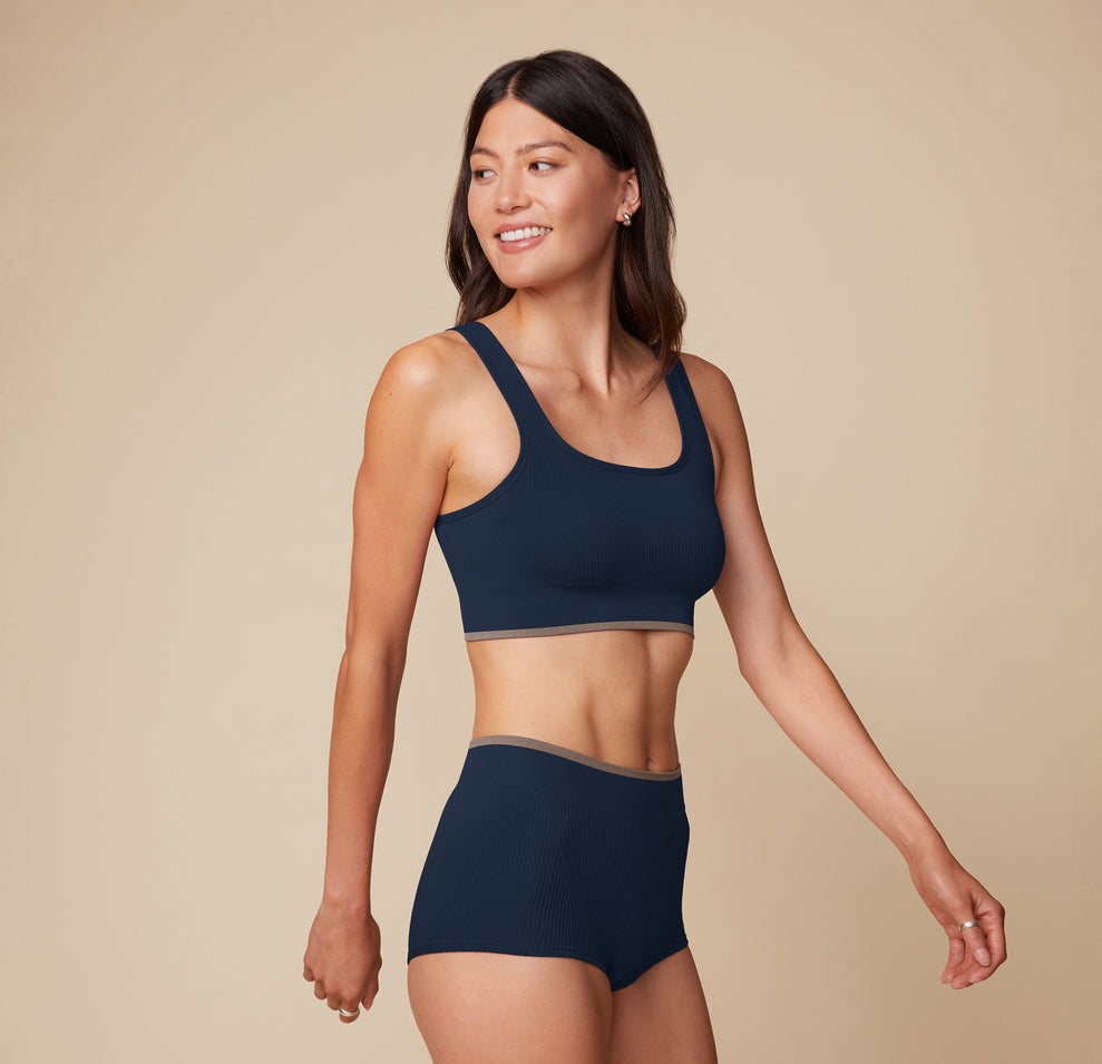 Side view of model Anna in the Lounge Scoop Bralette and Lounge Boyshort in True Blue, slightly angled with one arm swinging back, highlighting the ribbed fabric and comfy fit. sizing: Anna wears size Small