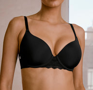 In a softly lit indoor setting, a model wears the Base Lace T-Shirt Bra in Black. The lightly lined underwire bra features smooth microfiber cups, adjustable straps, and soft lace trim along the front for an everyday look with a subtle detail.