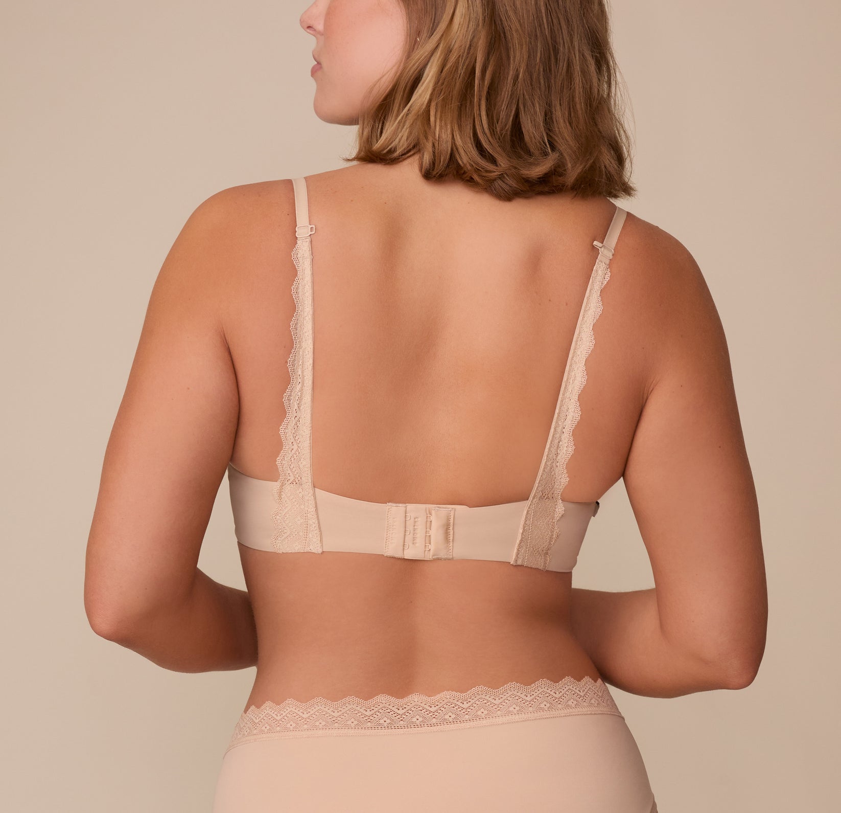 Sonnie shown from the back in the Base Lace T-Shirt Bra in Beige. The image captures the adjustable lace-trimmed straps and hook-and-eye closure, designed for comfort and convertibility with the J-hook racerback option.