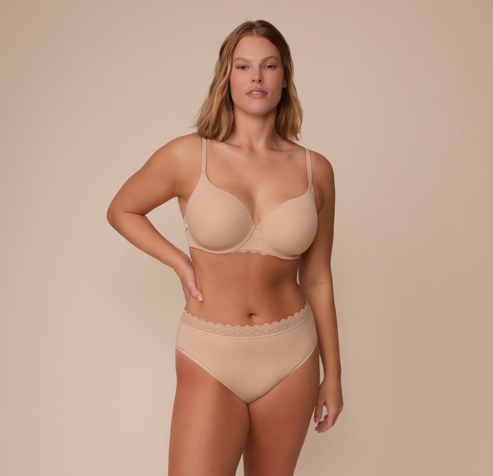 Sonnie standing front-facing in the Base Lace T-Shirt Bra and matching Bliss Lace Highwaist Brief in Beige. The full set showcases the ultra-soft microfiber fabric and scalloped lace accents designed for everyday comfort.