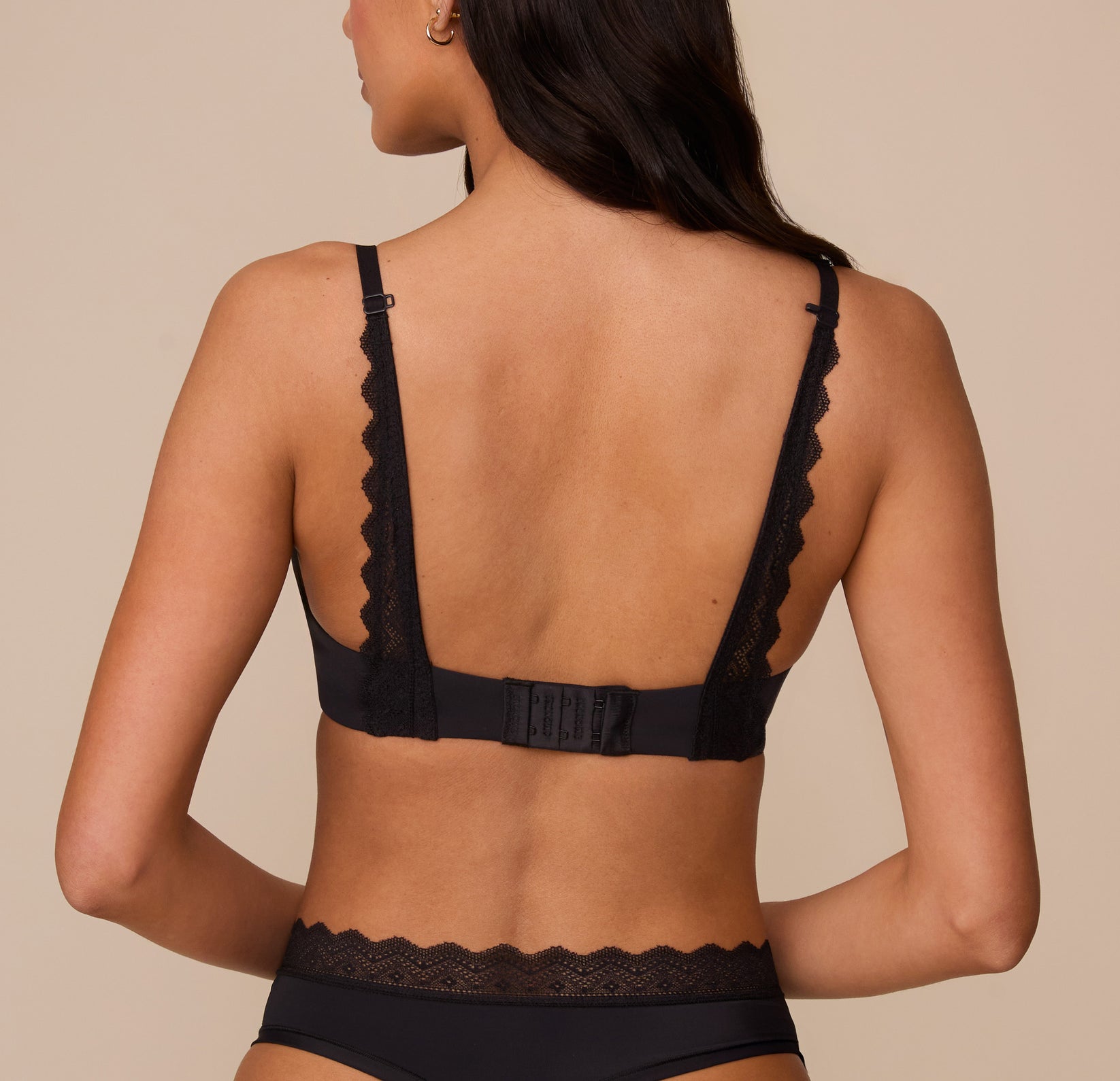 Marcela shown from the back in the Base Lace T-Shirt Bra in Black. The lace-trimmed straps and hook-and-eye closure are visible, offering support with convertible racerback capability.
