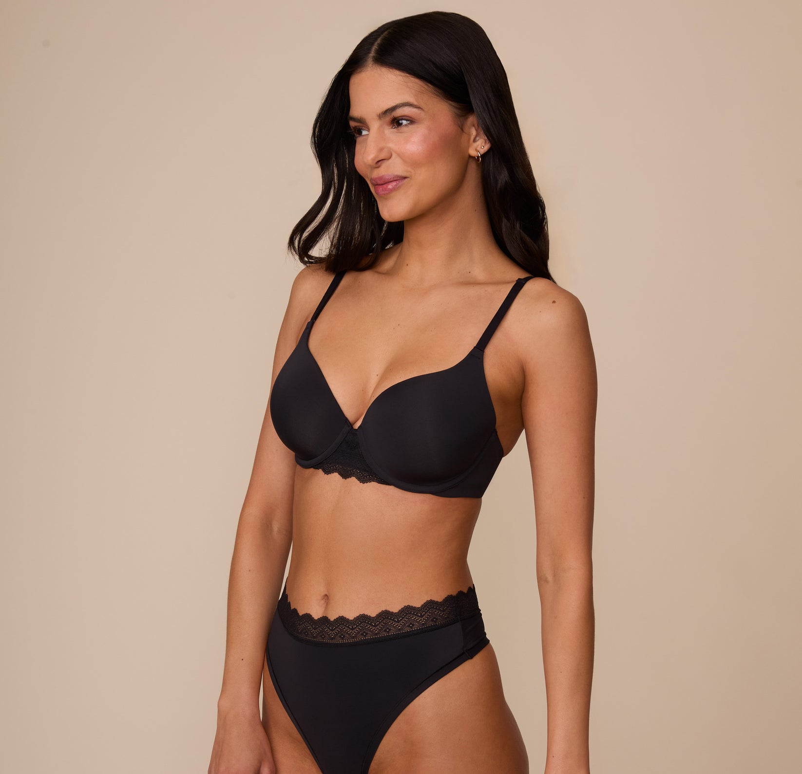 Marcela in a three quarter angle pose wearing the Base Lace T-Shirt Bra in Black with the matching Bliss Lace Highwaist Thong. The bra’s smooth microfiber cups and lace detailing are clearly highlighted.