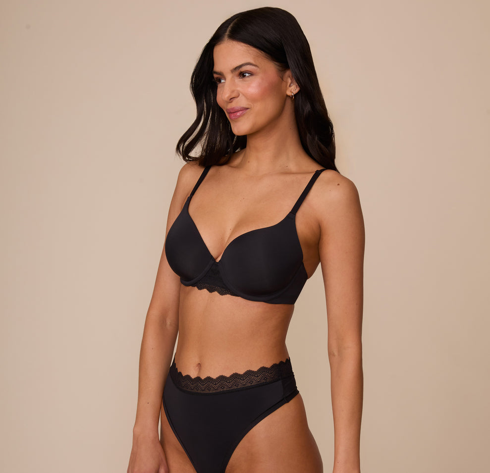 Marcela in a three quarter angle pose wearing the Base Lace T-Shirt Bra in Black with the matching Bliss Lace Highwaist Thong. The bra’s smooth microfiber cups and lace detailing are clearly highlighted.