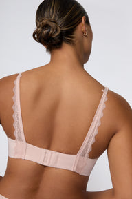 In a studio with a light gray backdrop, India wears the Base Lace Bra in Ember Rose from the back, highlighting the lace-trimmed straps, adjustable straps, and hook-and-eye closure.