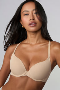 On a light grey studio backdrop, Amber wears the Base Push-Up Bra in Beige, shown from the waist up. The lightly lined underwire cups create lift and shape, with smooth microfiber fabric and thin adjustable straps. sizing: Amber wears size 32C