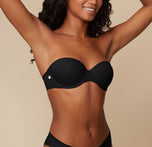 Three quarter view of Ally posing with her hands behind her head, modeling the Base Strapless Bra in Black against a simple, neutral background.