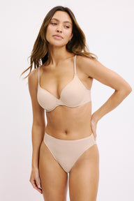 On a white studio backdrop, Darion wears the Base T-Shirt Bra in Beige with matching underwear, shown from the front to highlight the lightly lined underwire cups, smooth microfiber fabric, and adjustable straps.