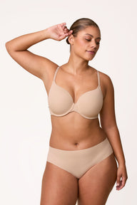 On a light neutral studio backdrop, India wears the Base T-Shirt Bra in Beige with matching underwear, shown from the front. The underwire design features lightly lined cups, front-adjusting straps, and breathable microfiber fabric for everyday comfort.