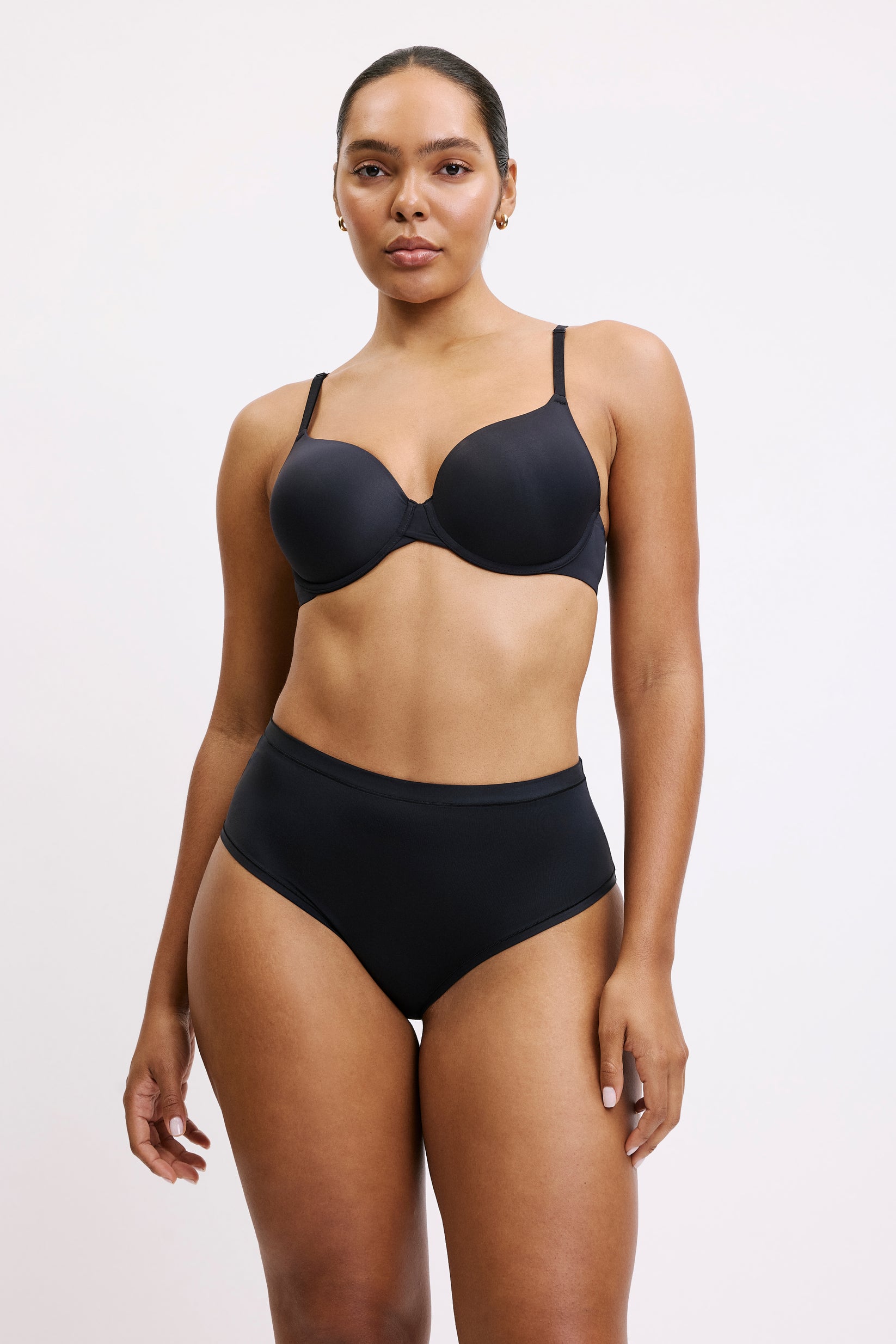 Against a light gray studio backdrop, Amber wears the Base T-Shirt Bra in Black with matching high-rise black underwear. The lightly lined, full-coverage cups create a smooth silhouette under thin front-adjusting straps, finished in Harper Wilde’s signature soft microfiber fabric.