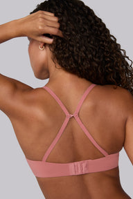 In a studio with a light gray backdrop, Courtney wears the Base T-Shirt Bra in Cinnamon from the back, showing the sliding J-hook racerback conversion, adjustable straps, and hook-and-eye closure.