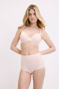 On a white studio backdrop, Megan wears the Base T-Shirt Bra in Rose, shown from the front with lightly lined underwire cups and thin adjustable straps in smooth microfiber fabric.