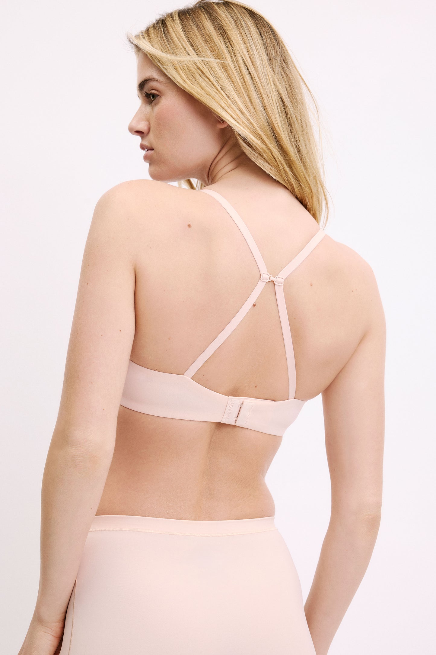 On a white studio backdrop, Megan wears the Base T-Shirt Bra in Rose, shown from the back with the J-hook converted to a racerback and a smooth microfiber band.
