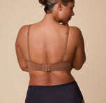India showcases the back of the Base T-Shirt Bra in Brown, emphasizing the adjustable hook-and-eye closure and slim, supportive straps.