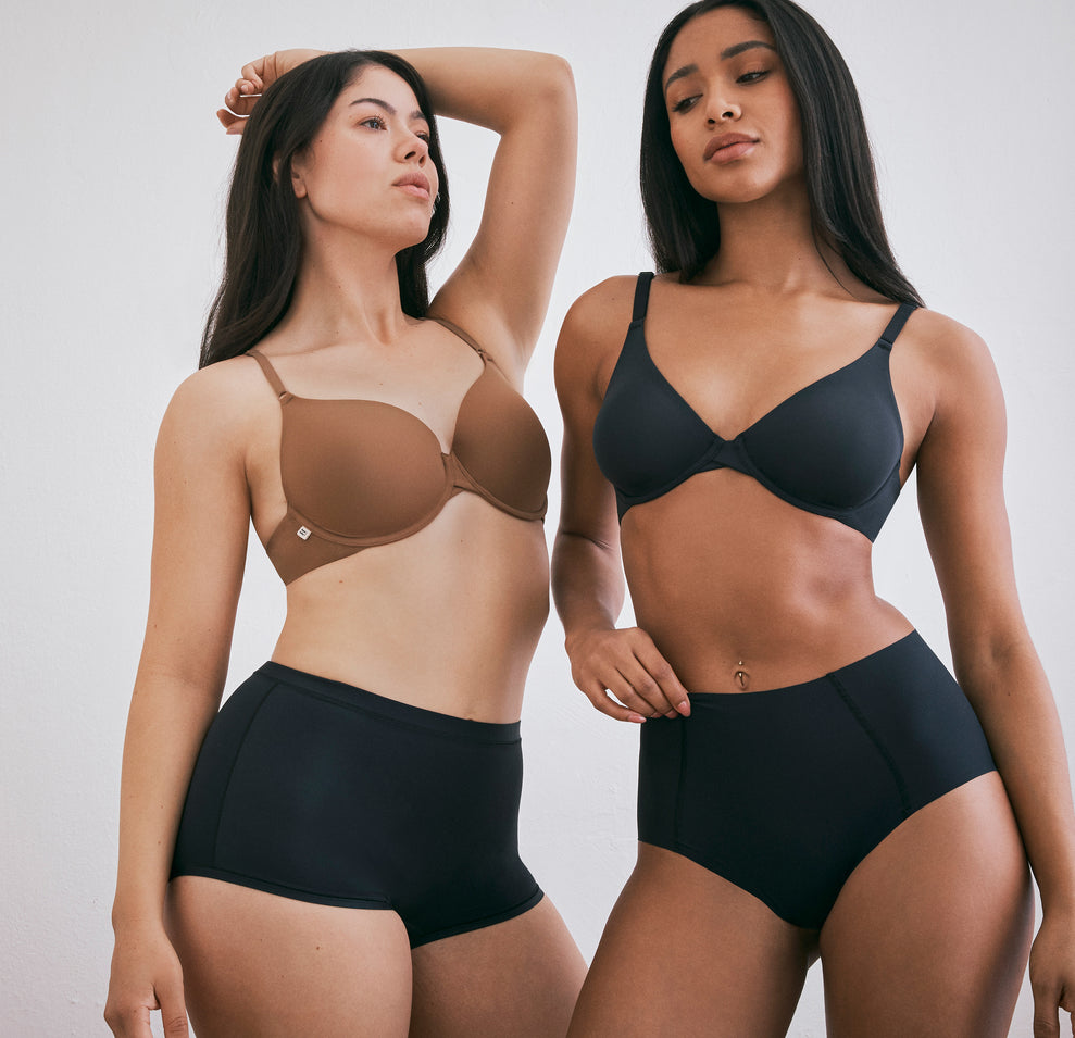 Emersyn and Ally model different shades of the Base T-Shirt Bra, with Emersyn wearing the Base T-Shirt Bra in Brown and Ally wearing the same bra in black, posing together to highlight the range of color options.