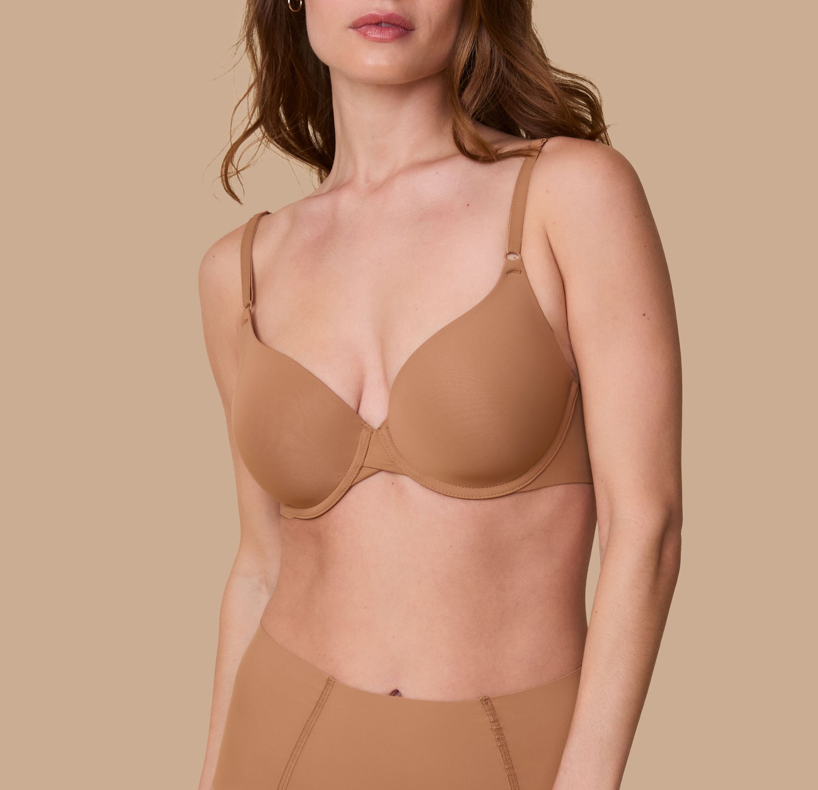 Gracie models the Base T-Shirt Bra in Tan, showcasing a front view of the bra's smooth, seamless design with lightly padded cups and adjustable straps. sizing: Gracie wears size 32D