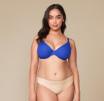 laudia smiling while wearing the Base Unlined Bra in Deja Blue paired with the No-Show Bikini in Beige. The front view highlights the vibrant color and supportive design of the bra. sizing: Claudia wears size 34DDD/F