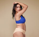 A side profile of Claudia wearing the Base Unlined Bra in Deja Blue and the No-Show Bikini in Beige.