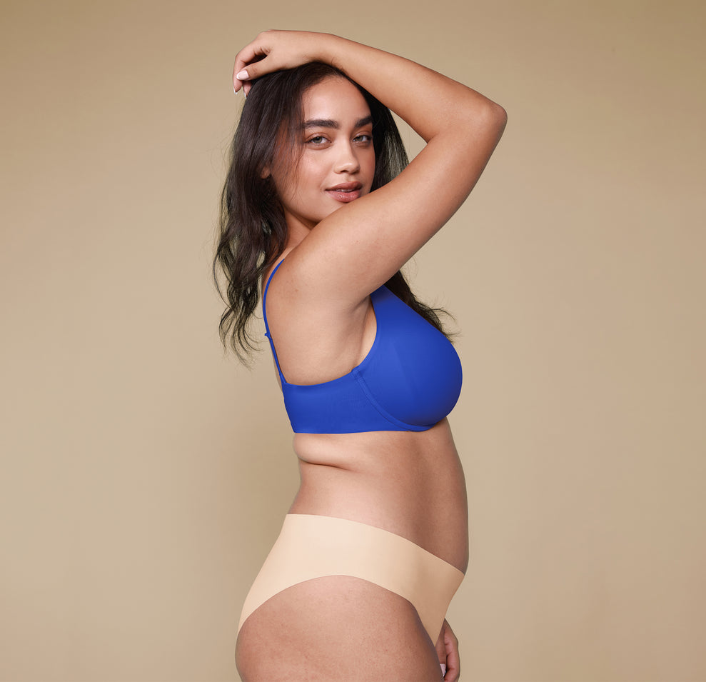 A side profile of Claudia wearing the Base Unlined Bra in Deja Blue and the No-Show Bikini in Beige.