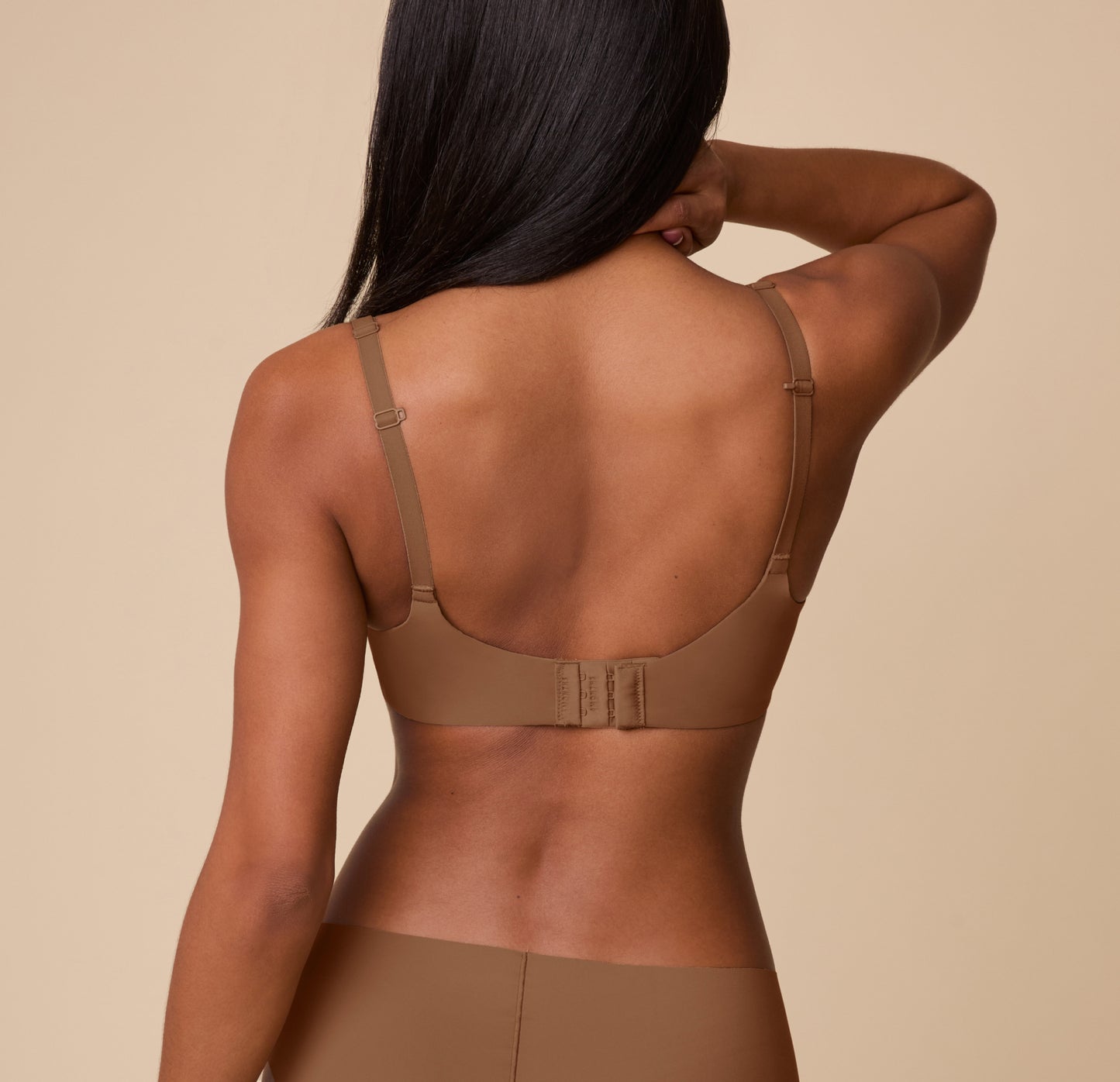 Back view of Ally wearing the Base Unlined Bra in Brown, showcasing the adjustable straps and hook-and-eye closure on the wide, smooth band.