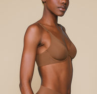 Three quarter view of Mariah wearing the Bliss Unlined Bra in Brown. The natural contour of the cups and comfortable front adjusting straps are highlighted.