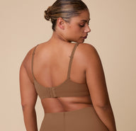 Back view of India wearing the Base Unlined Bra in Brown, emphasizing the racerback-convertible J-hook and smooth microfiber finish.