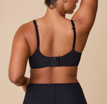A back view of India wearing the Base Unlined Bra in Black, highlighting the adjustable straps and hook-and-eye closure.