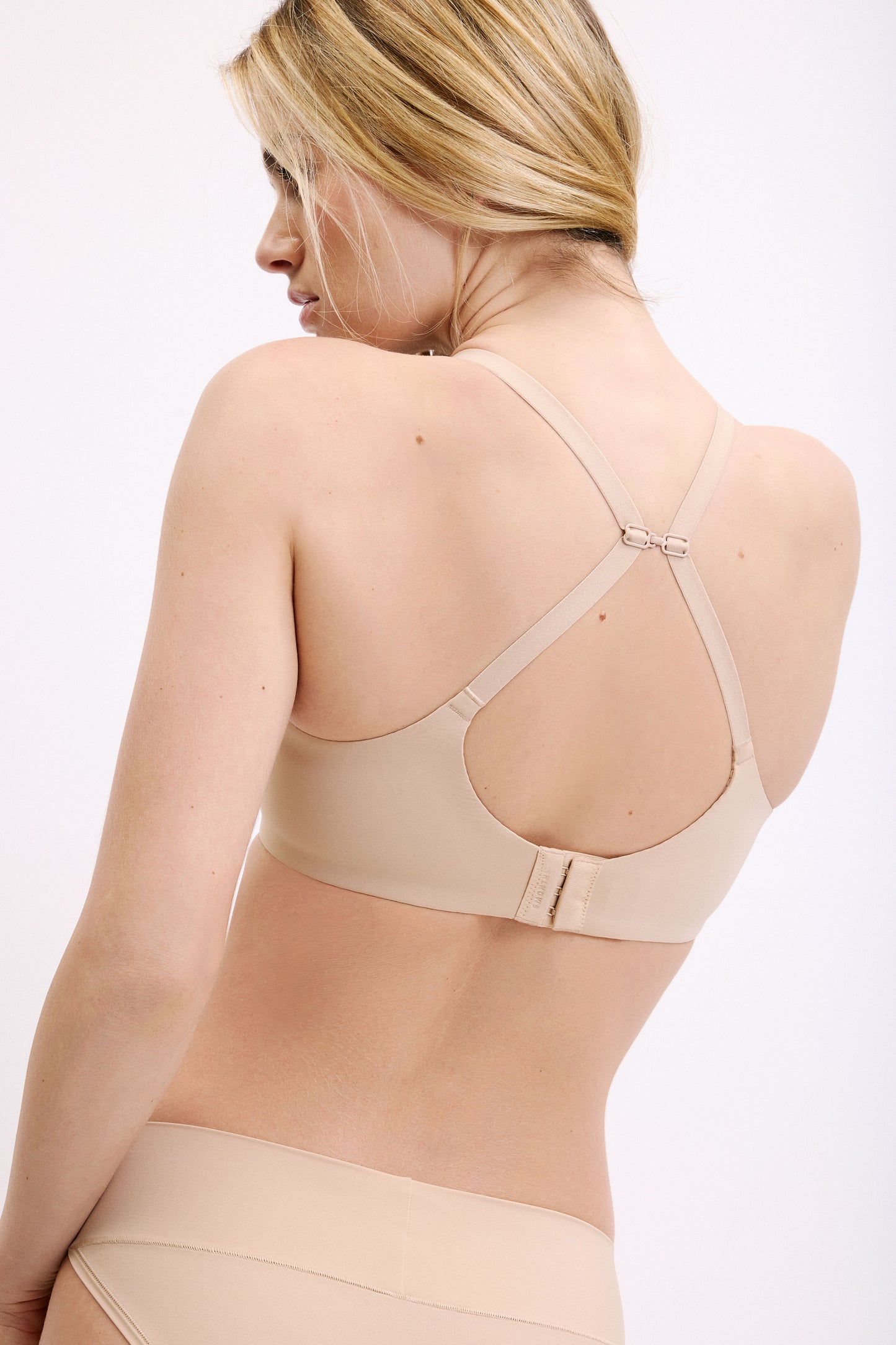 On a white studio backdrop, Megan wears the Base Unlined Bra in Beige, showing the flexible underwire, unlined cups, and clean, everyday silhouette.