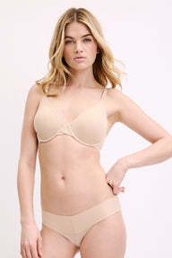 On a white studio backdrop, Megan wears the Base Unlined Bra in Beige with matching bottoms, showing the unlined cups, flexible underwire, and smooth microfiber fabric.