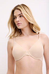 On a white studio backdrop, Megan wears the Base Unlined Bra in Beige, highlighting the unlined cups, natural V neckline, and adjustable straps. sizing: Megan wears size 32D