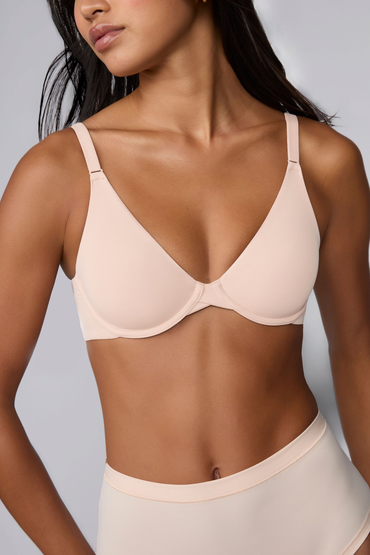 In a studio with a light gray backdrop, Amber wears the Base Unlined Bra in Rose, showing the unlined underwire cups, smooth microfiber fabric, and front-adjusting straps. sizing: Amber wears size 32C