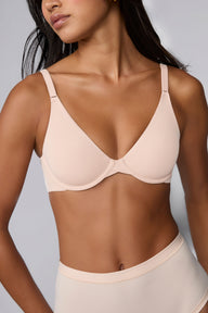 In a studio with a light gray backdrop, Amber wears the Base Unlined Bra in Rose, showing the unlined underwire cups, smooth microfiber fabric, and front-adjusting straps. sizing: Amber wears size 32C