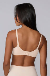 In a studio with a light gray backdrop, Amber wears the Base Unlined Bra in Rose from the back, highlighting the smooth microfiber band, adjustable straps, and hook-and-eye closure.