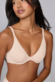 In a studio with a light gray backdrop, Amber wears the Base Unlined Bra in Rose, showing the unlined underwire cups, front-adjusting straps, and smooth microfiber fabric.